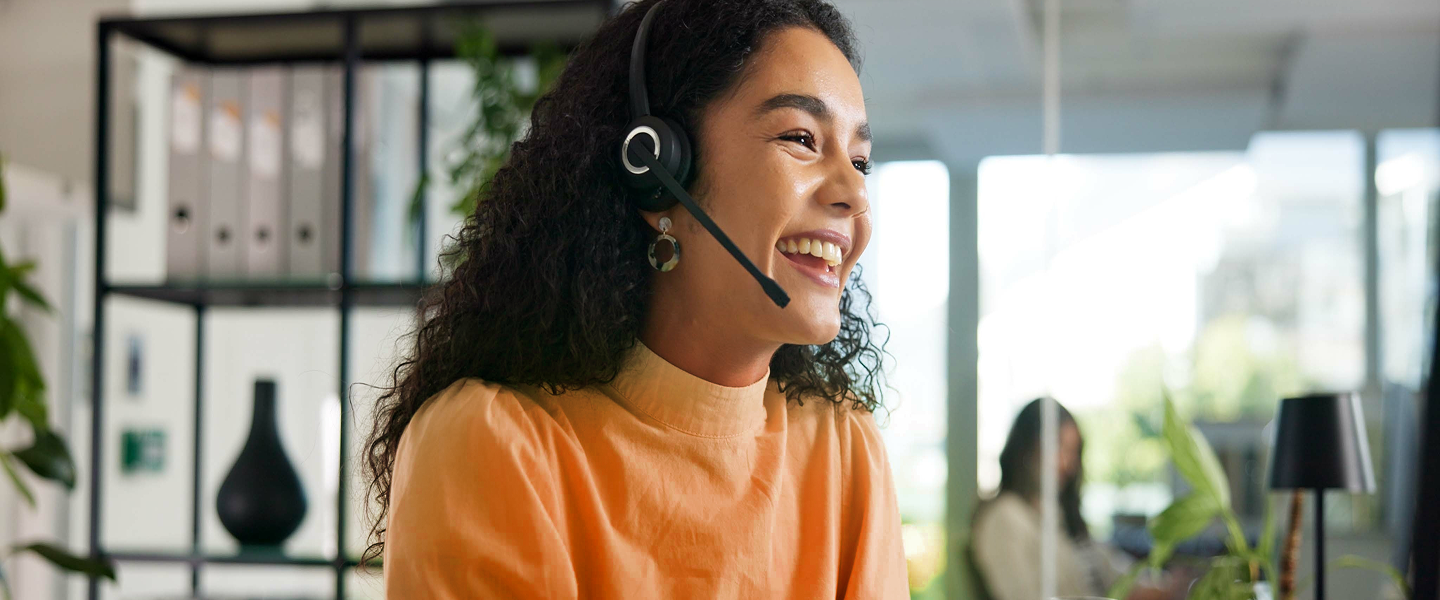 Smiling woman and child with red hair hugging on a sandy beach near an orange boat with a mountain in the background.