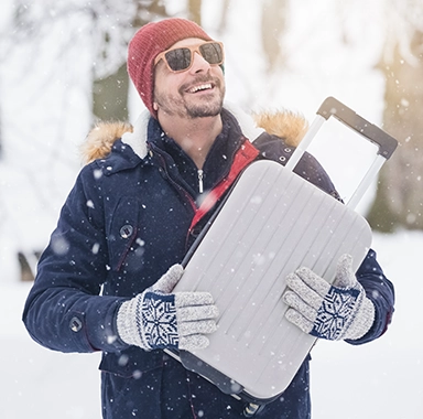 un homme porte une valise sous la neige, il est heureux d'être parti en vacances en décembre
