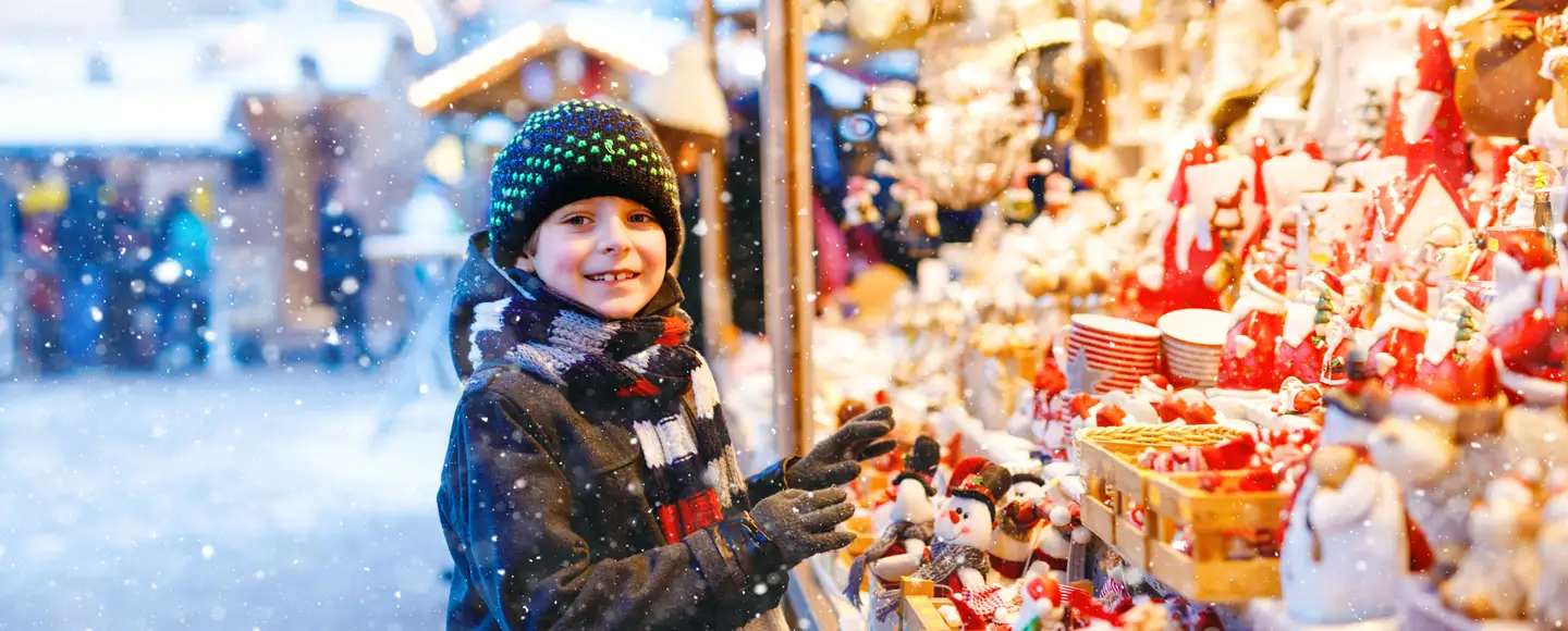 un enfant est devant une boutique à un marché de Noël sous la neige, il est heureux d'être parti en vacances en Décembre