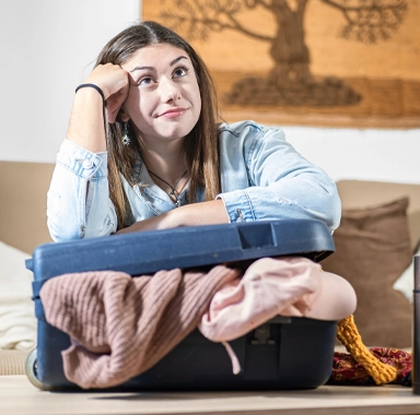 une jeune femme prépare sa valise pour partir en vacances en février mais elle a des difficultés pour la fermer. elle a souscrit une assurance voyage 