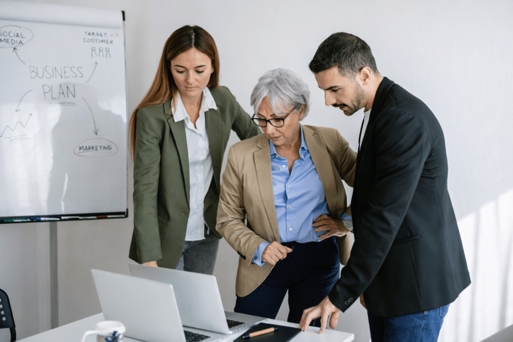 Trois collaborateurs de générations différentes analysent un projet sur ordinateur, illustrant la posture professionnelle et la collaboration intergénérationnelle en entreprise.