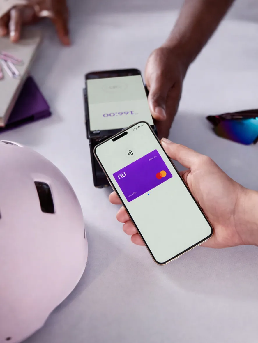 Person holding a smartphone displaying a purple digital card, making a contactless payment on a card reader held by another person.