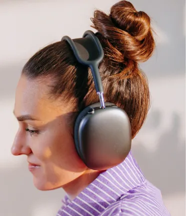 Profile of a woman with brown hair in a bun wearing large black over-ear headphones.