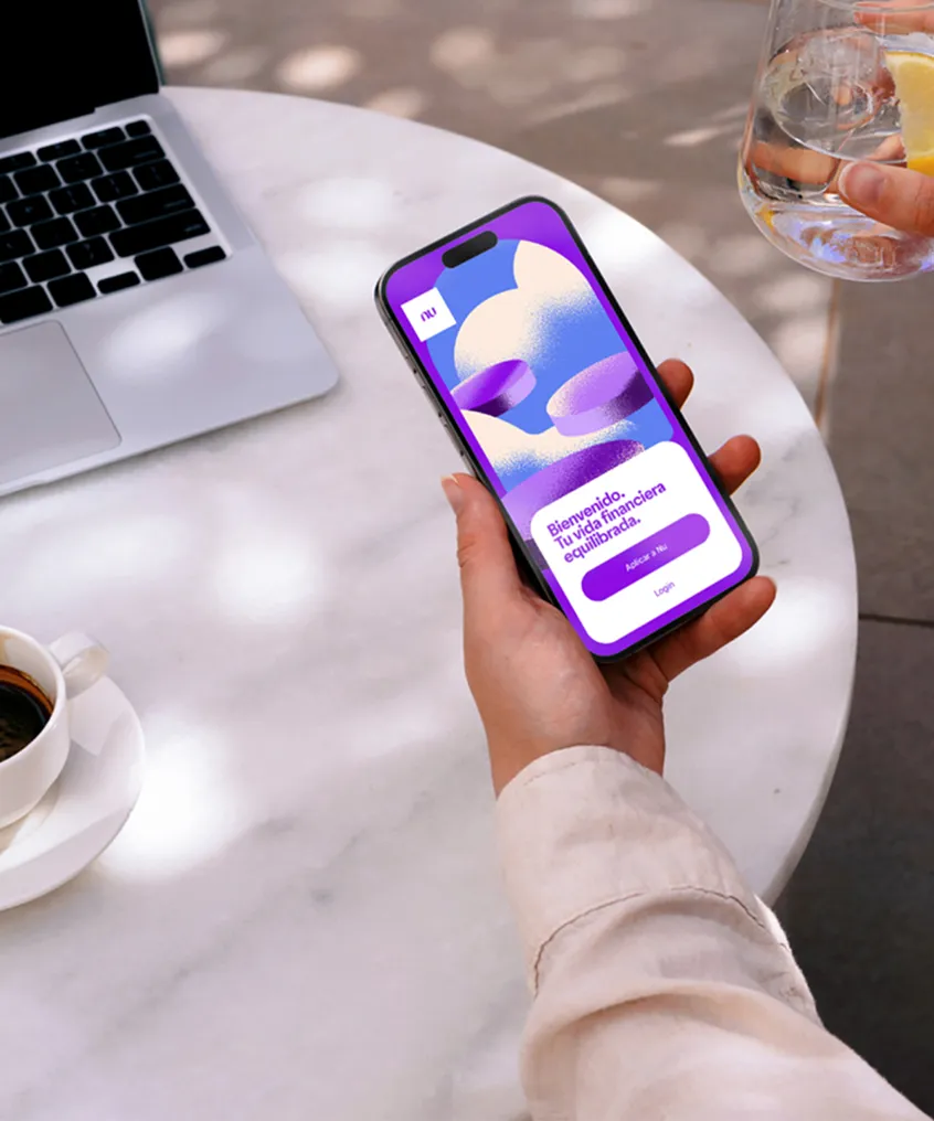 Person holding a smartphone displaying a package tracking app with a hot air balloon graphic, near a glass of water with lemon and a laptop on a round table.