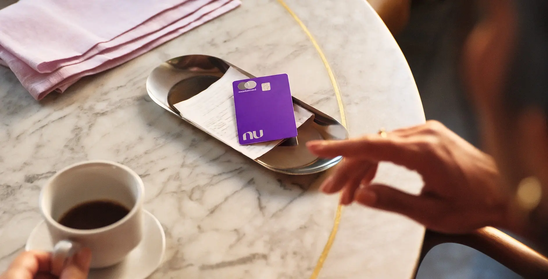 Smiling woman with earrings and purple straps holding her hair back against a clear blue sky.