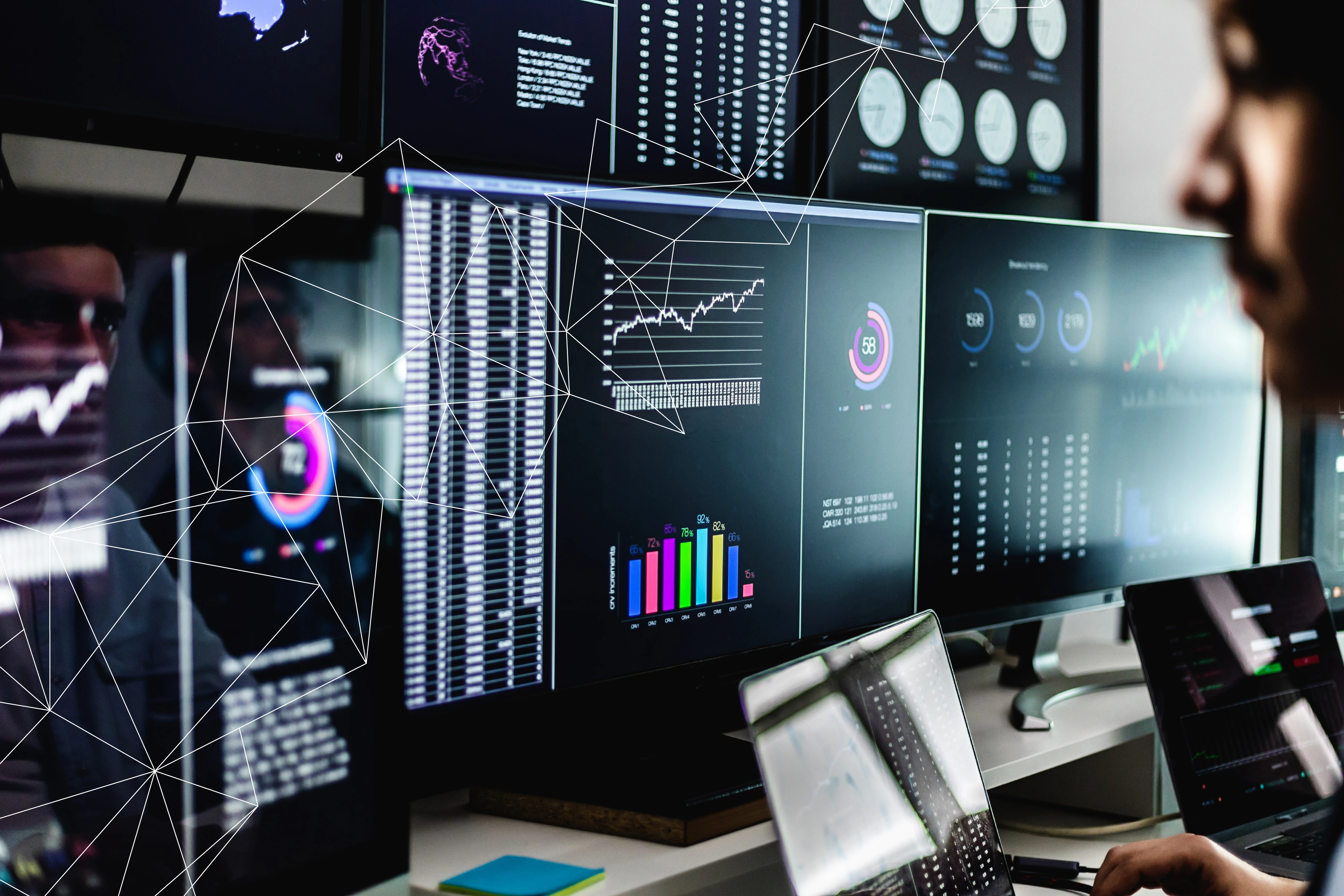 Person analyzing multiple data screens showing charts, graphs, and statistics on computers and laptops.