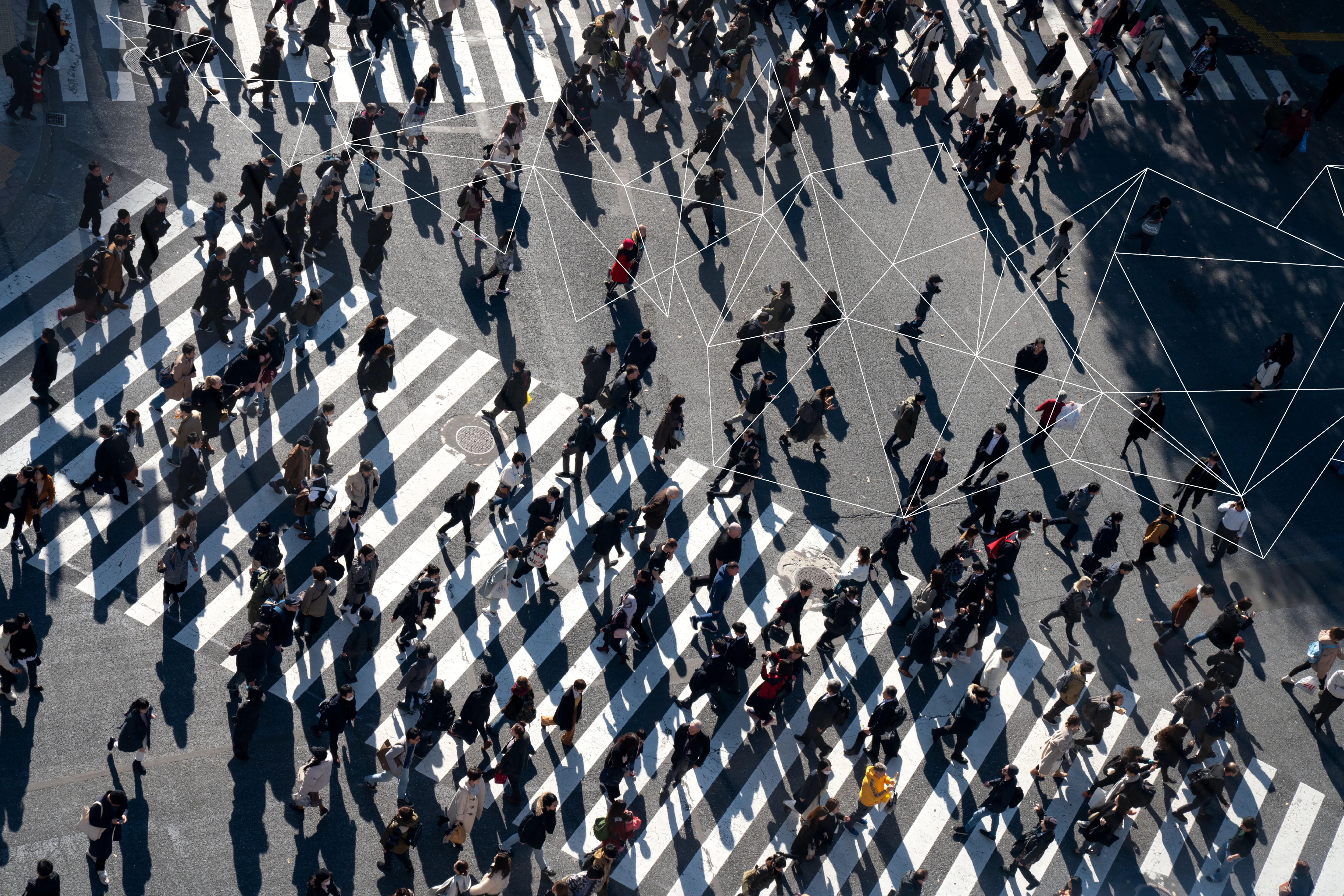Aerial view of crowded crosswalk with people casting long shadows and connected network lines overlaid.