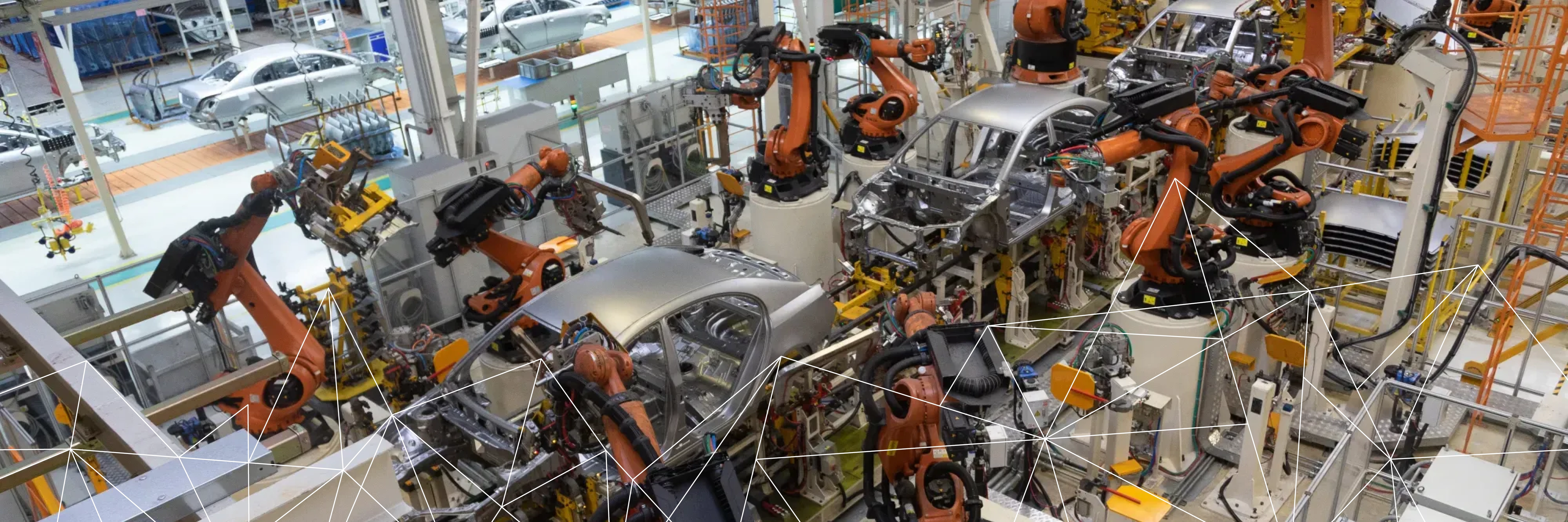 Automated robotic arms assembling silver car bodies in a modern automotive manufacturing plant.