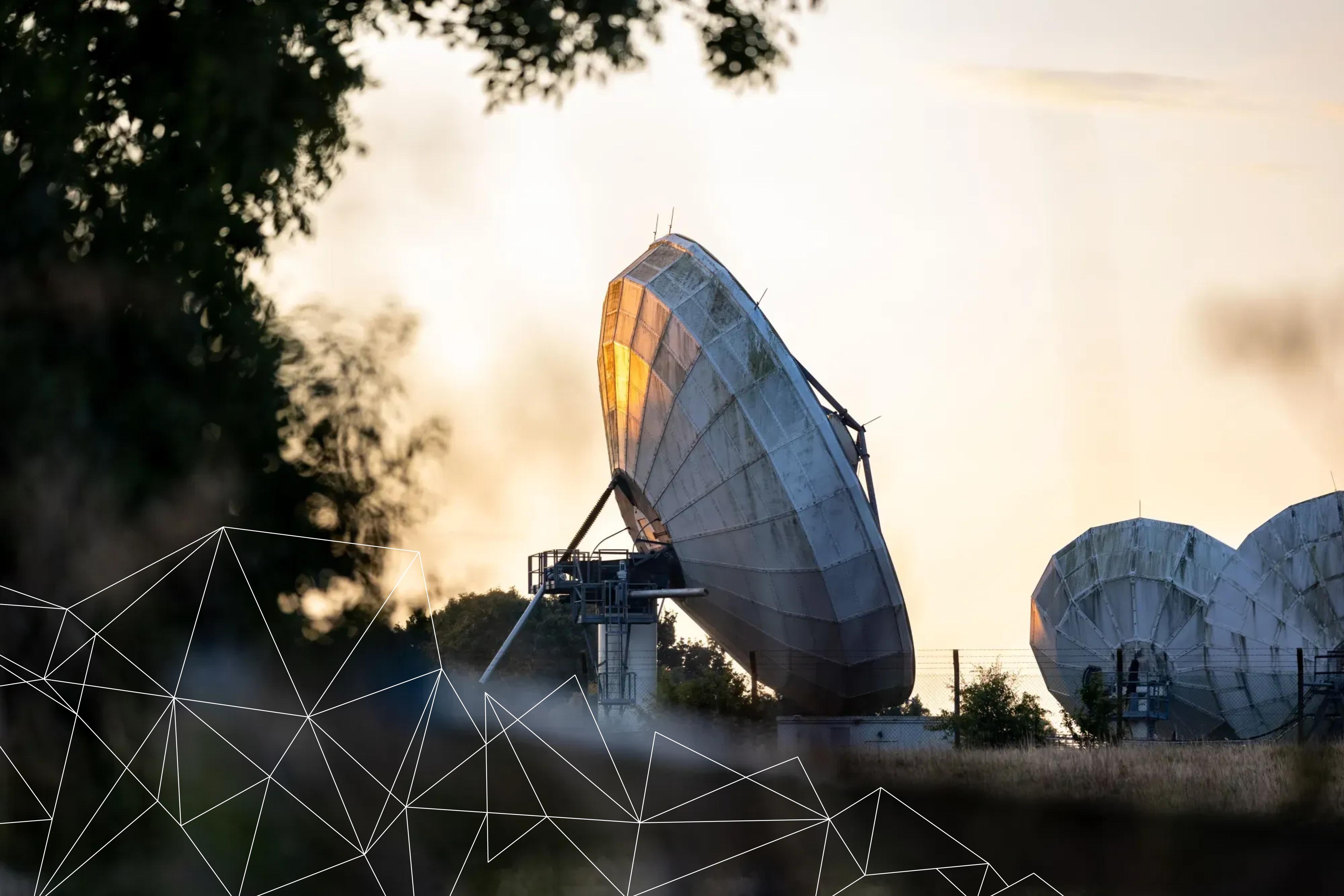 Large satellite dishes in a field at sunset reflecting golden light.