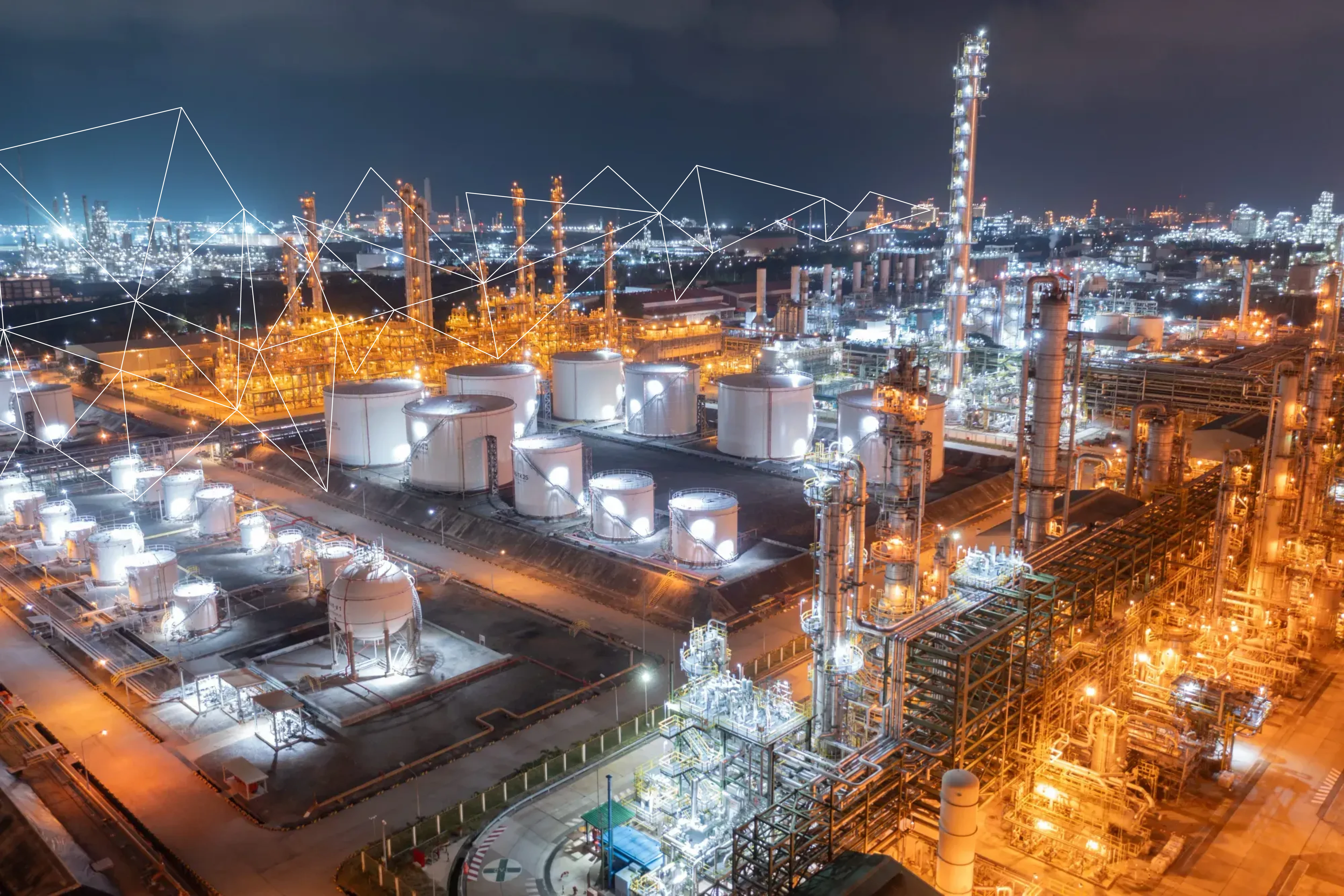 Night view of a brightly lit petrochemical refinery with tanks and tall distillation towers.