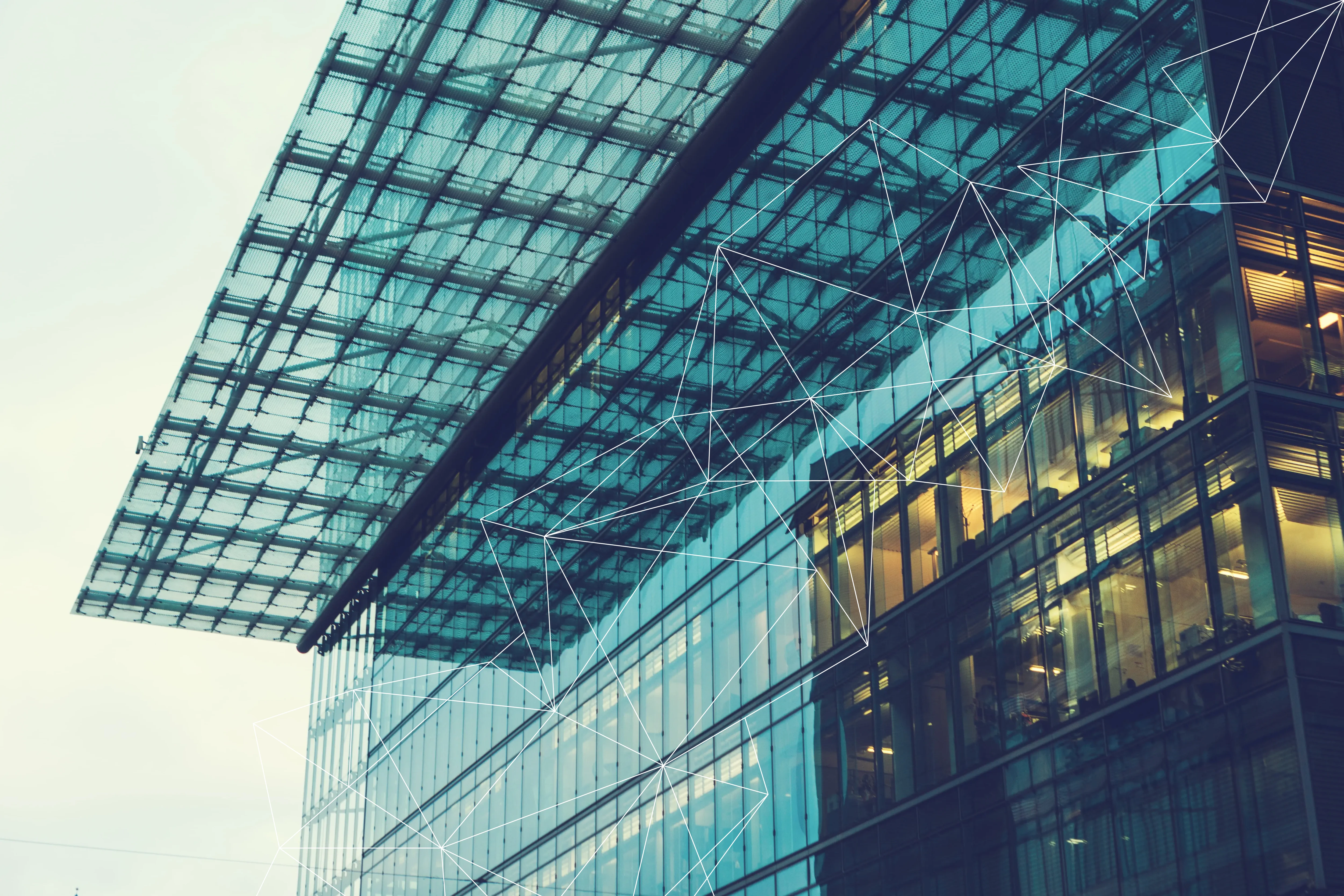 Modern glass office building with lit interiors and a transparent canopy roof at dusk.