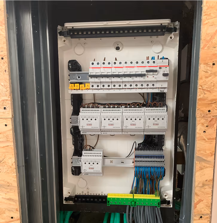 Open electrical panel with circuit breakers, wiring terminals, and connected cables organized inside a metal frame.
