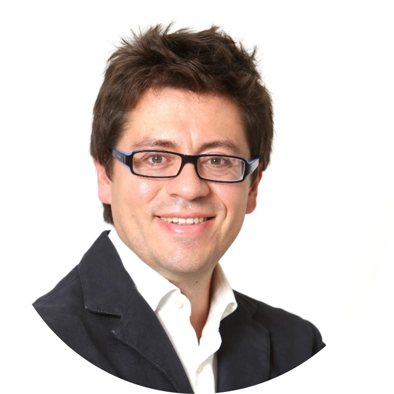 Smiling man with spiky dark hair wearing glasses, a white shirt, and a dark blazer against a white background.