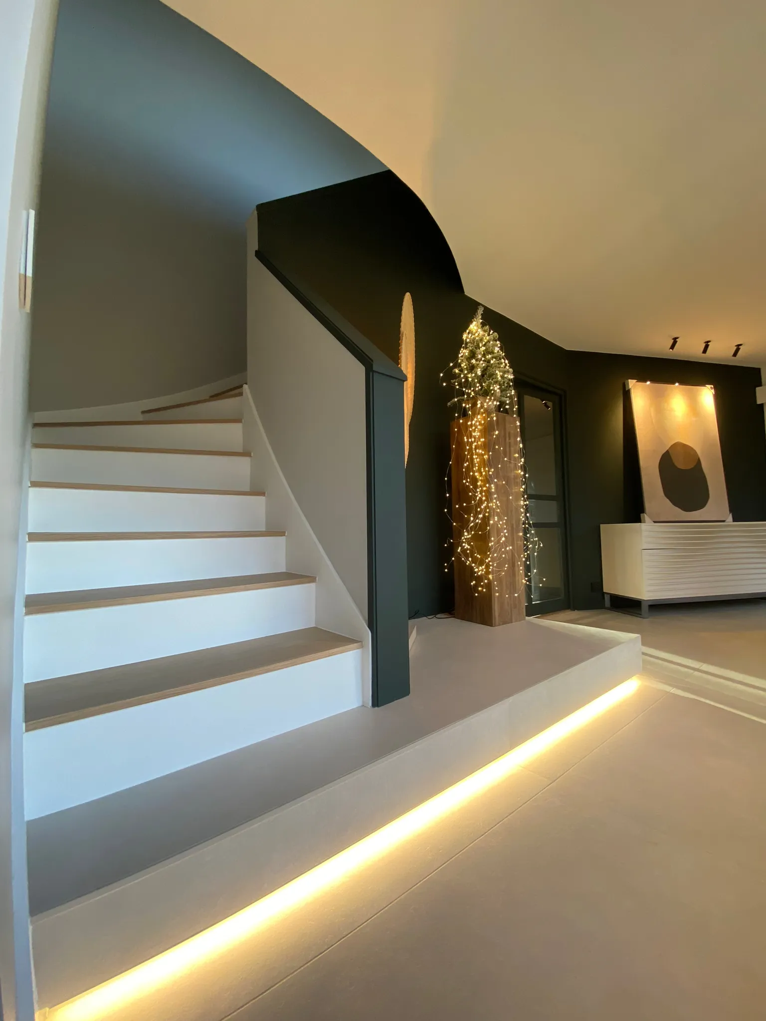 Modernisation d'une entrée des années 2000 : remplacement du carrelage bleu par un sol minéral et création d'un escalier suspendu en bois à Bondues.