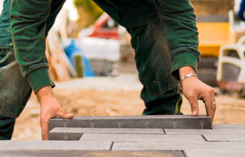 Person laying rectangular gray paving stones on the ground with both hands.