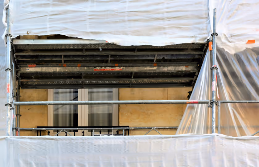 Building facade with window partially covered by scaffolding and protective white plastic sheeting during renovation.