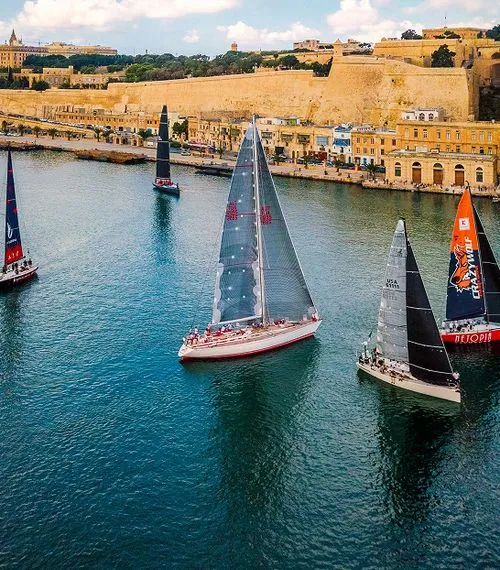 The image captures a moment during the Rolex Middle Sea Race, a renowned offshore yacht race that starts and finishes in Malta. 