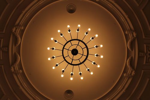 Kružni luster s više žarulja na dekorativnom stropu.