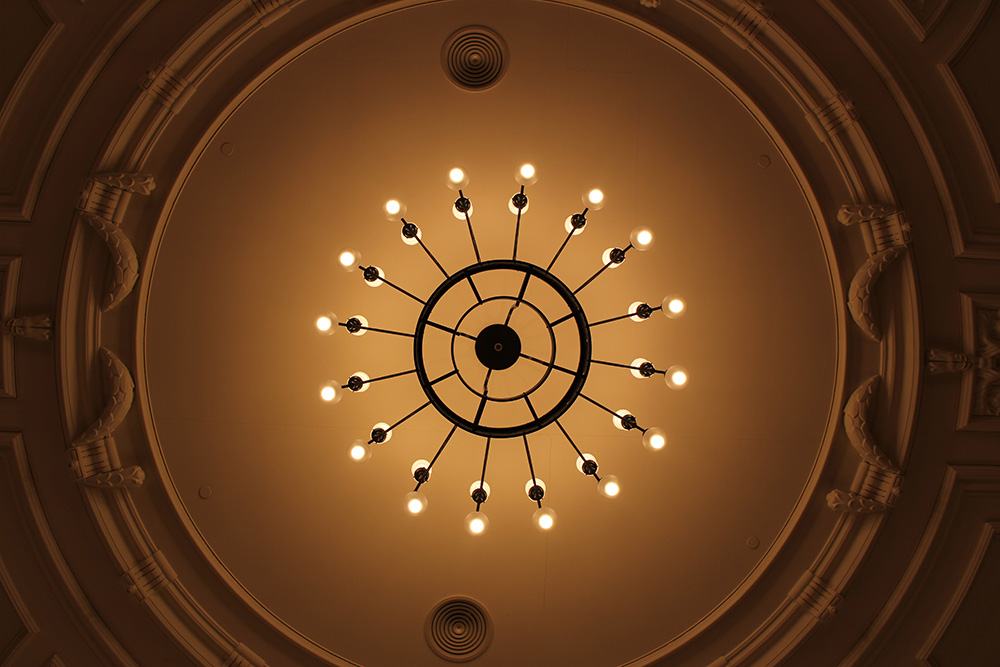 Kružni luster s više žarulja na dekorativnom stropu.