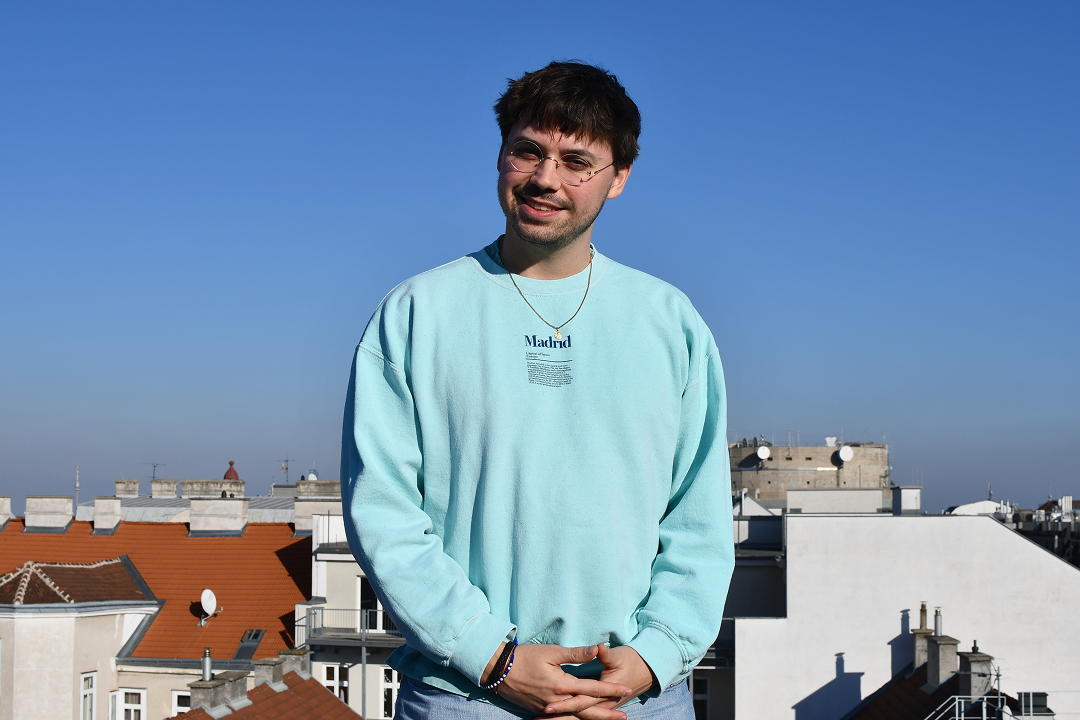 Florian Prasky mit Brille im türkis Pullover auf Dach vor blauem Himmel