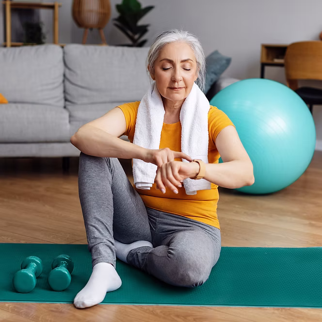 Foto einer Frau auf einer Yogamatte, die ihre Smartwatch bedient