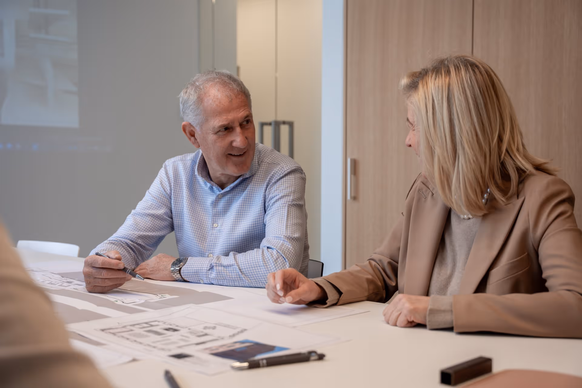 Twee professionals van Ars Interiors bespreken bouwtekeningen aan een tafel in een modern kantoor.