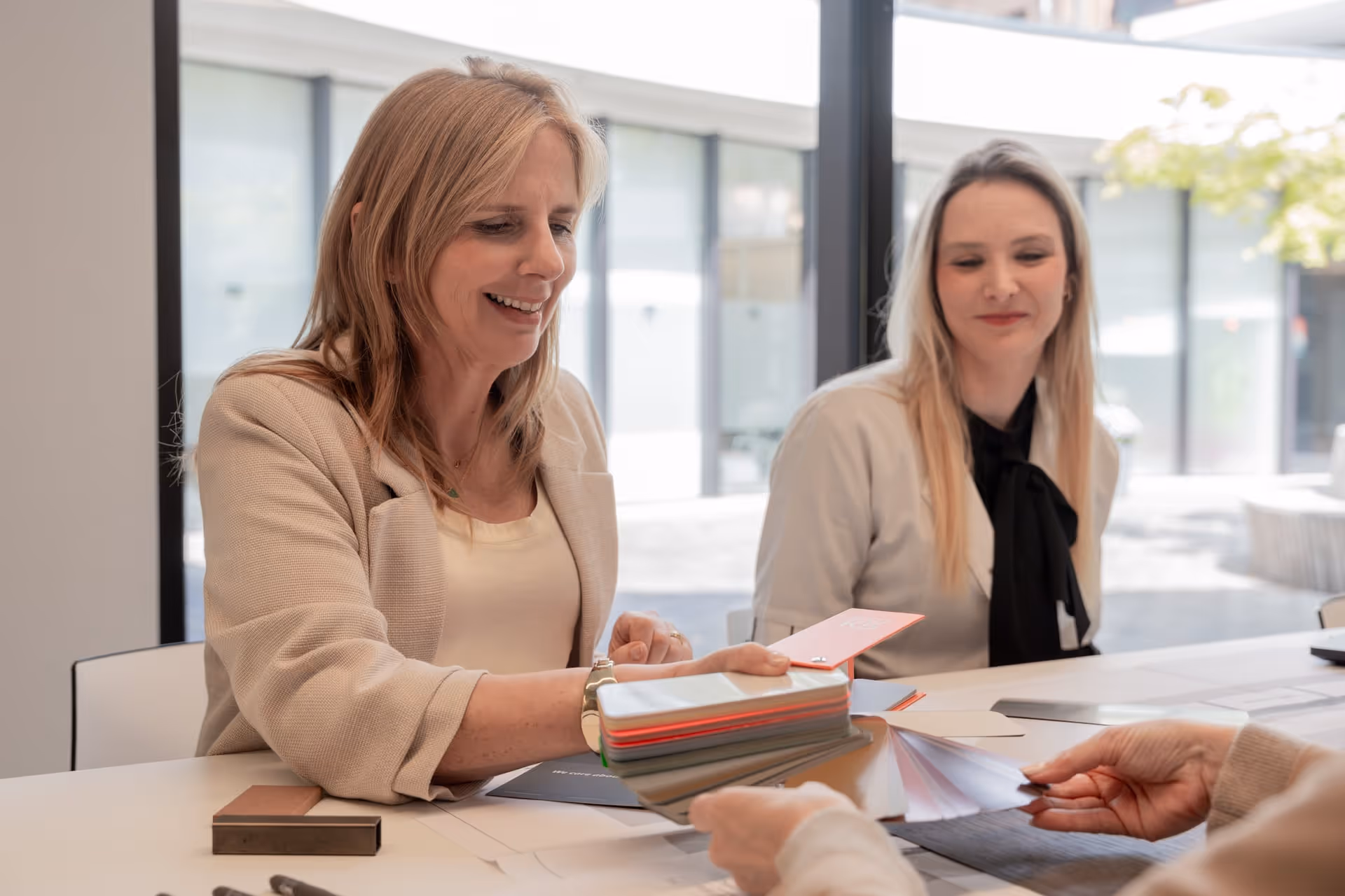 Twee vrouwen die kleurafbeeldingen en kleurstalen bekijken aan een tafel in een licht, modern kantoor.