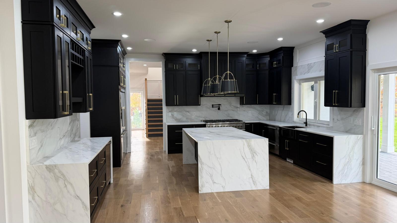 Modern kitchen with black cabinets, white marble countertops and island, hardwood floors, and pendant lighting.