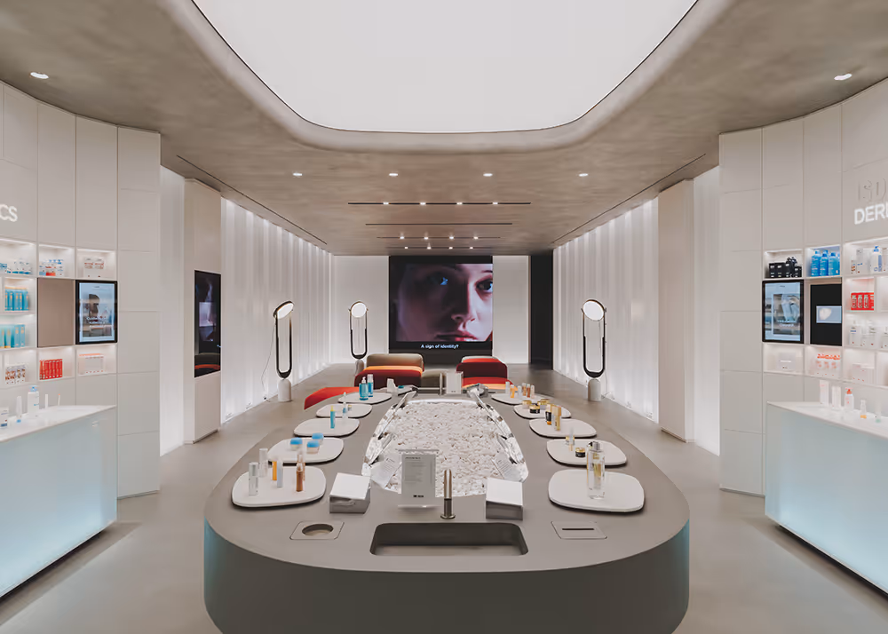 Interior moderno de una tienda de cuidado de la piel con mostradores iluminados, exhibición central de productos y una pantalla grande con el rostro de una persona.