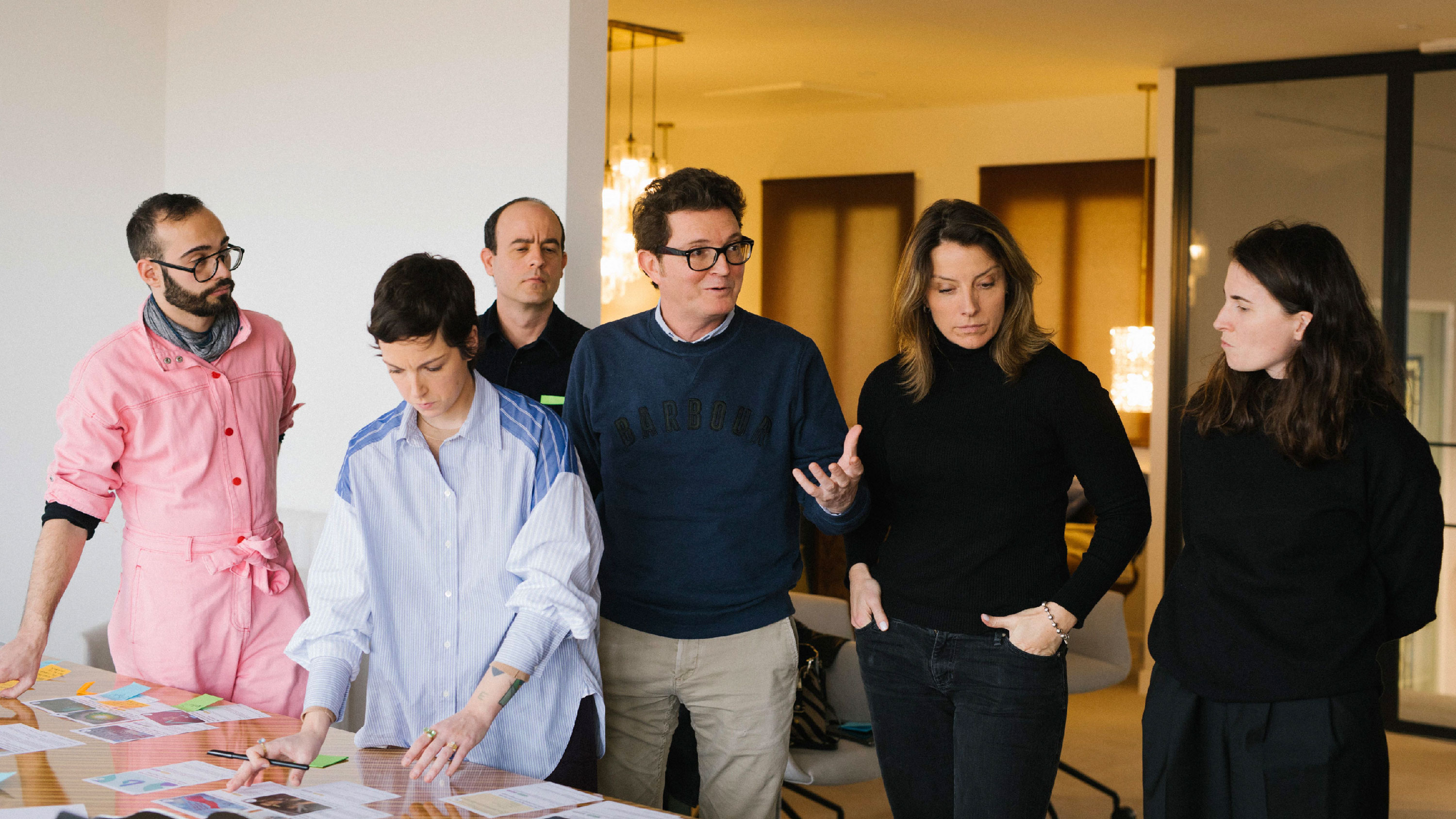 Seis personas adultas discuten y revisan documentos sobre una mesa en una habitación iluminada.