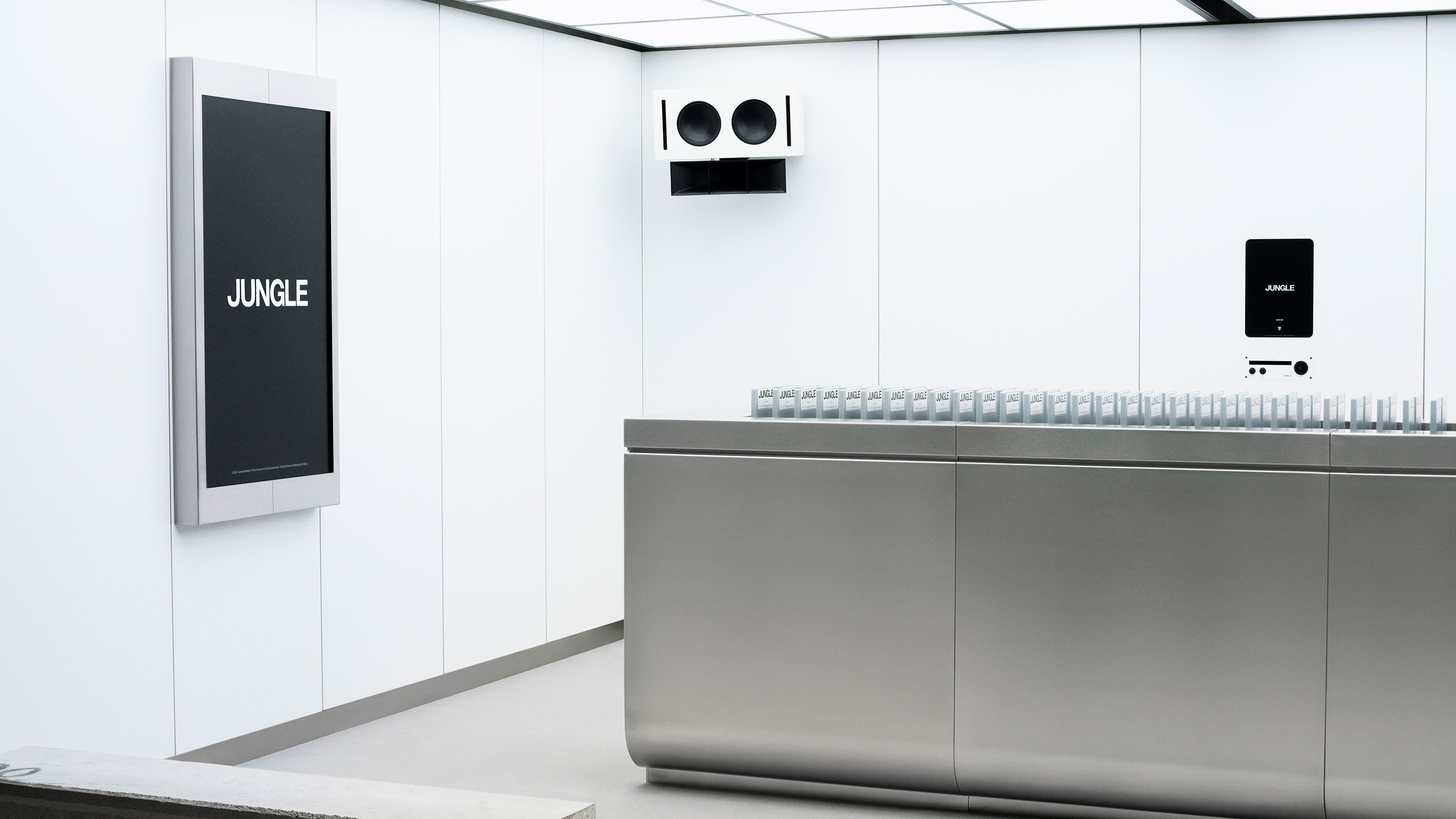 Recepción minimalista con mostrador metálico y pantallas que muestran la palabra 'Jungle' en un entorno blanco.