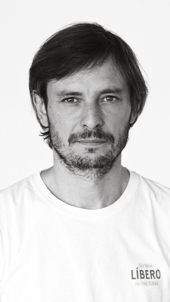 Retrato en blanco y negro de un hombre con barba y melena corta, vistiendo una camiseta blanca con texto en el pecho.
