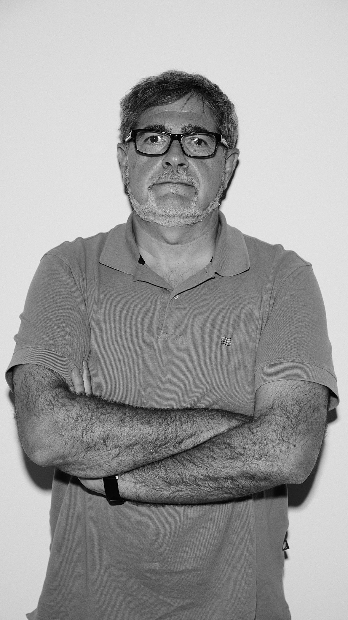 Hombre de mediana edad con gafas negras y barba canosa, con los brazos cruzados y camiseta tipo polo.