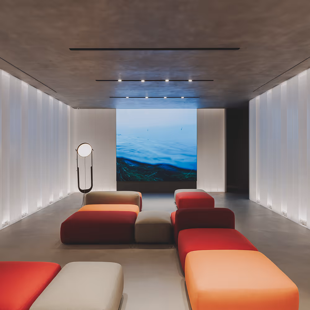 Sala moderna con sofás modulares en tonos rojos y naranjas, lámpara de pie circular y pantalla con imagen de agua.