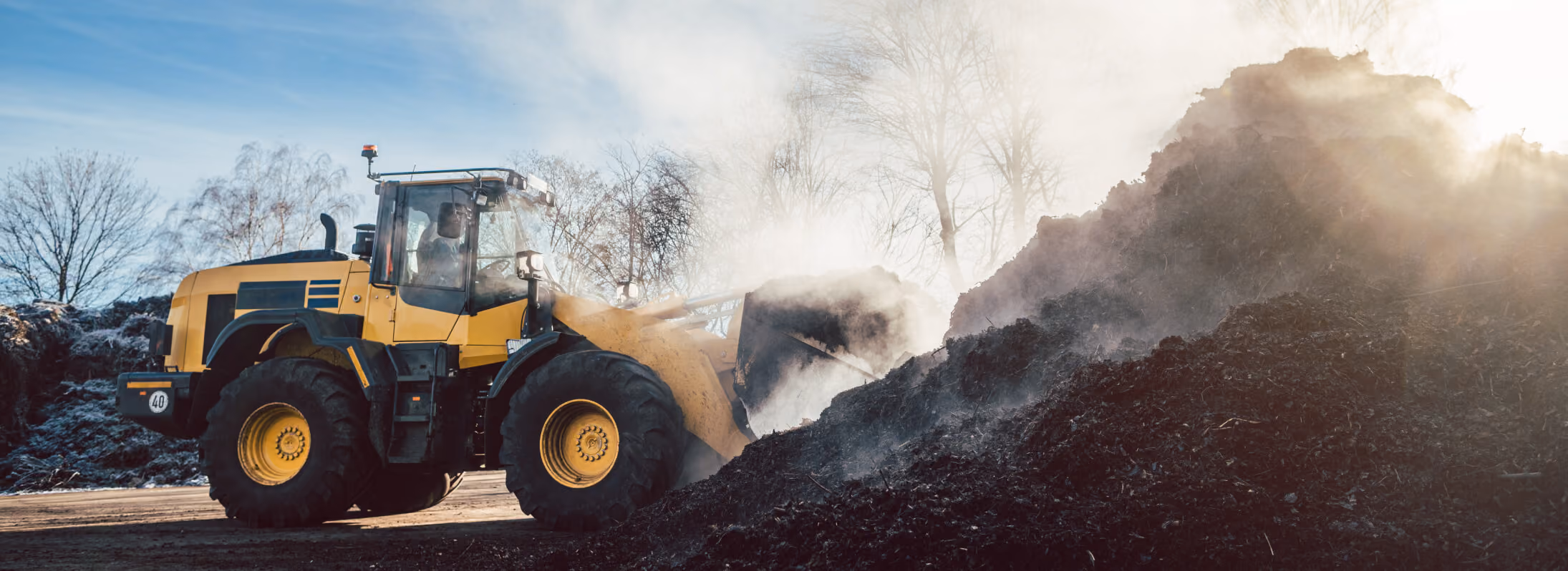 Tractor moving large pile of mulch with dust circling around