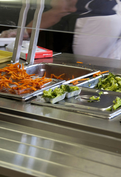 Serving trays with sweet potato fries and broccoli at a cafeteria food counter.