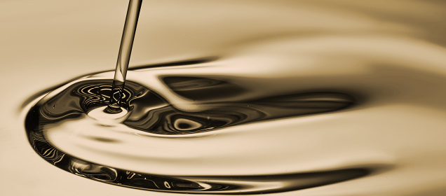 Close-up of a smooth liquid stream pouring into reflective, rippling liquid creating circular waves.