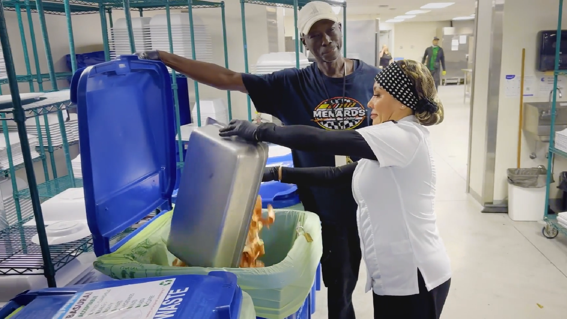 Man holding open trash bin while women dumps unused food.