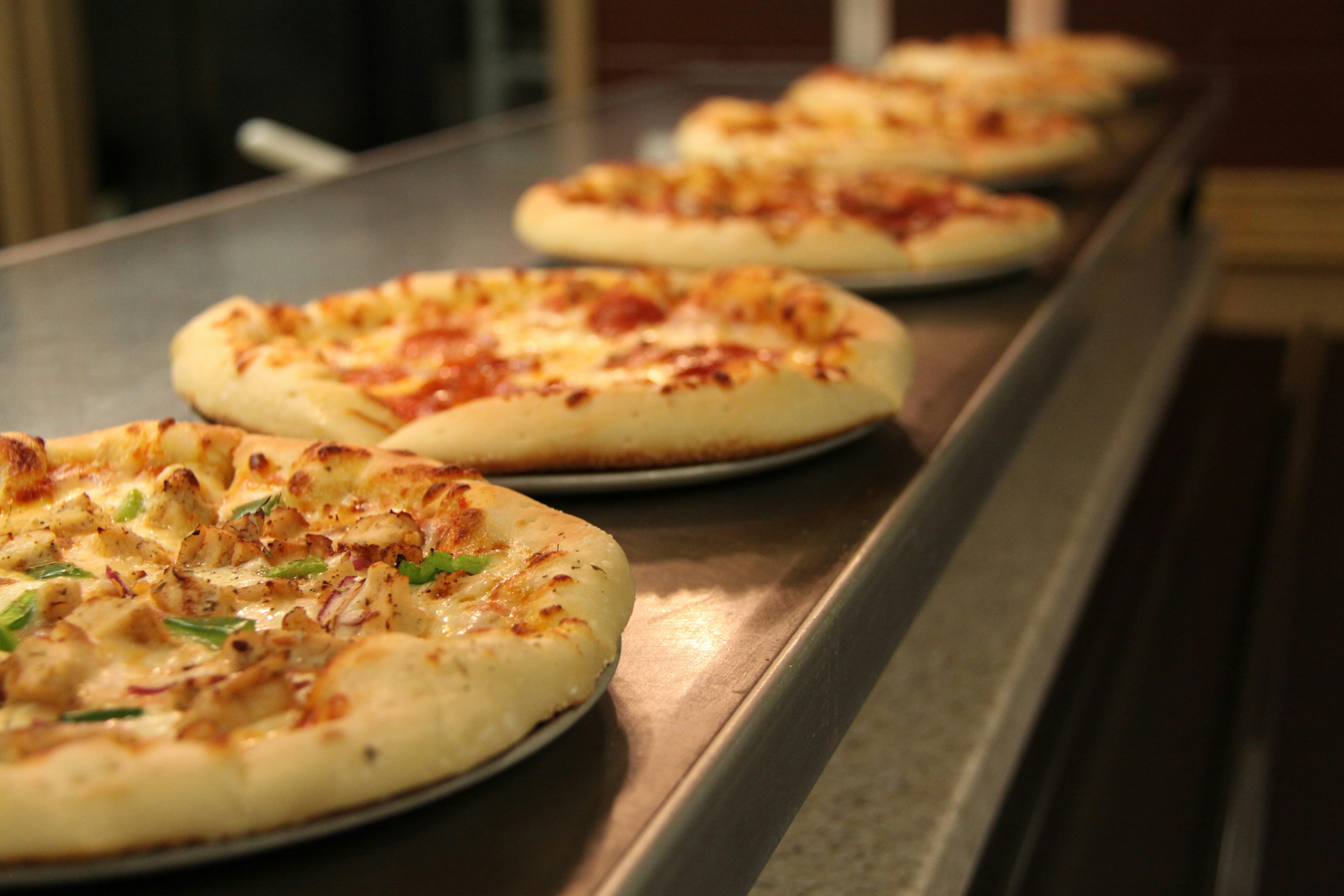 Row of Pizzas waiting on a metal counter