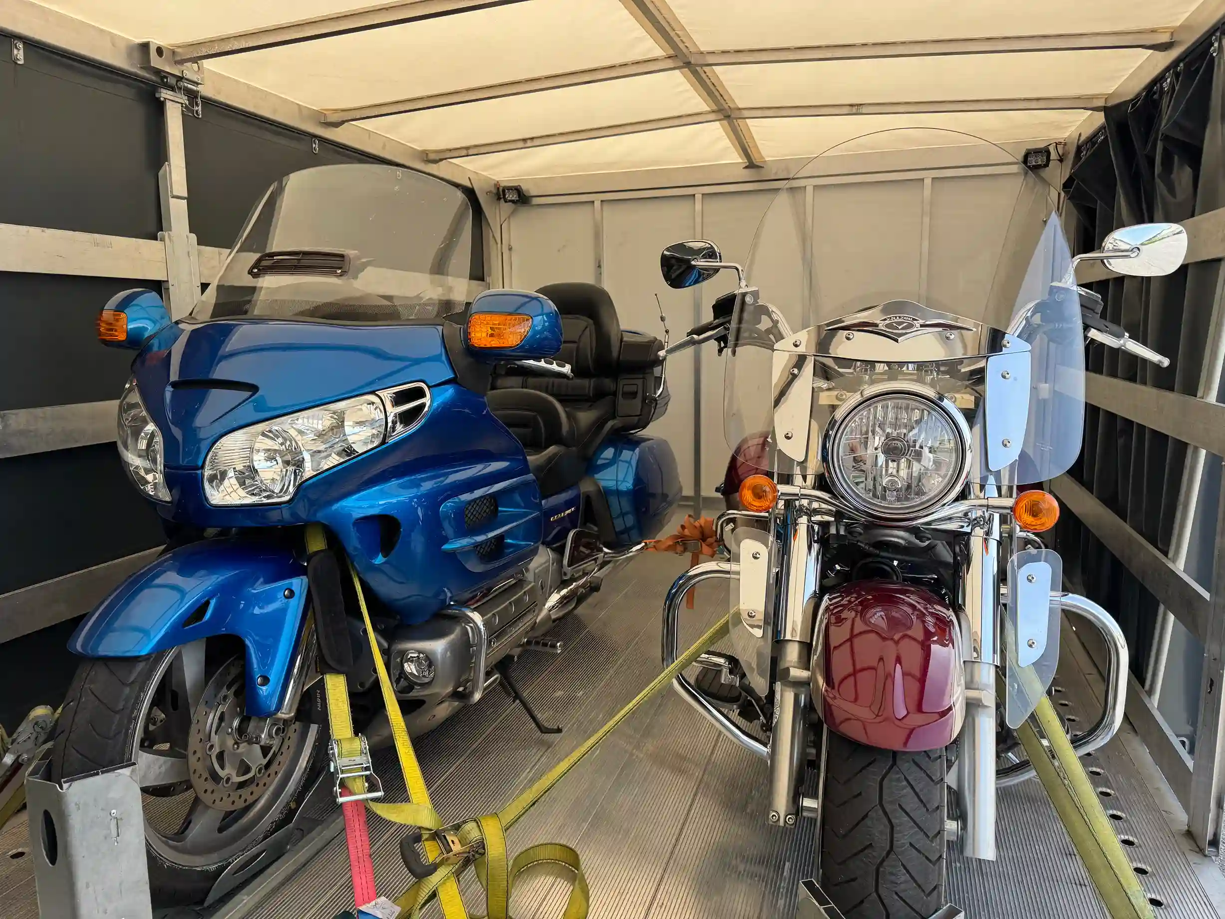 One blue and one red motorcycle secured in an enclosed trailer.