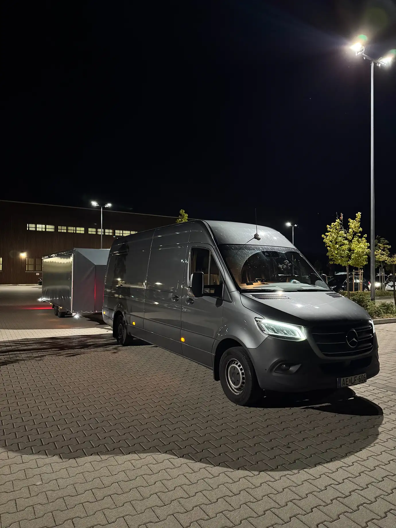 Grey van and enclosed trailer parked in the lot at night.