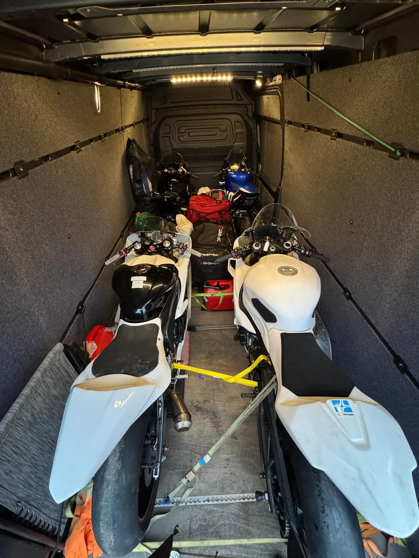 Four road motorcycles and riding gear secured with straps, viewed from above.