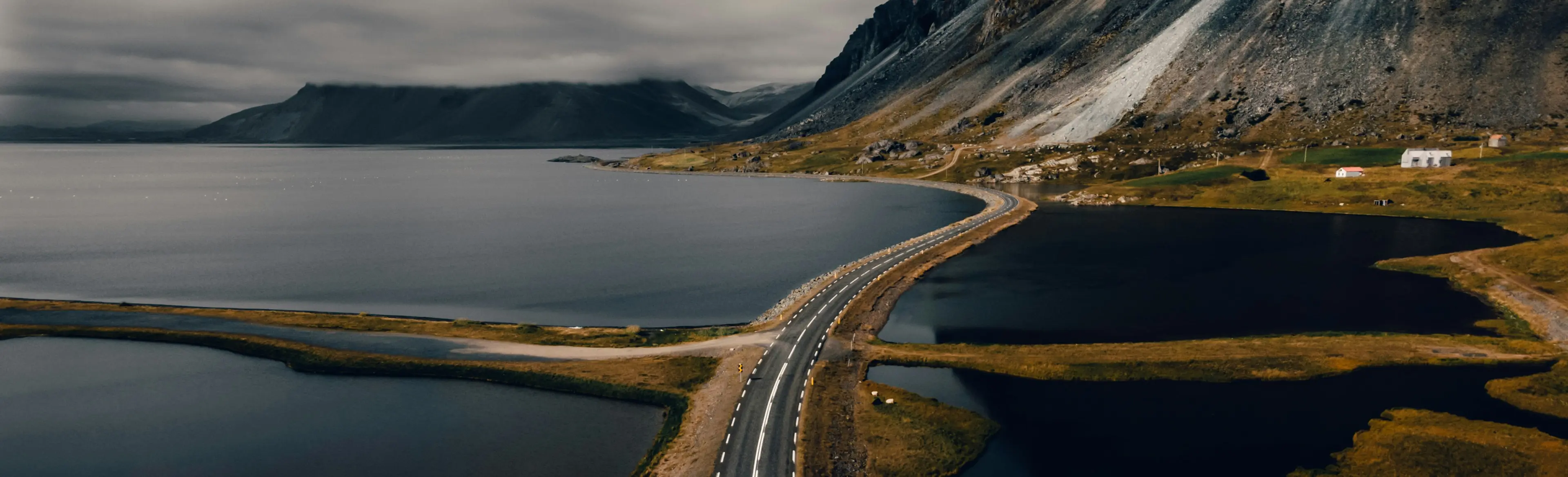 Asphalt road crossing open water with mountains in the background