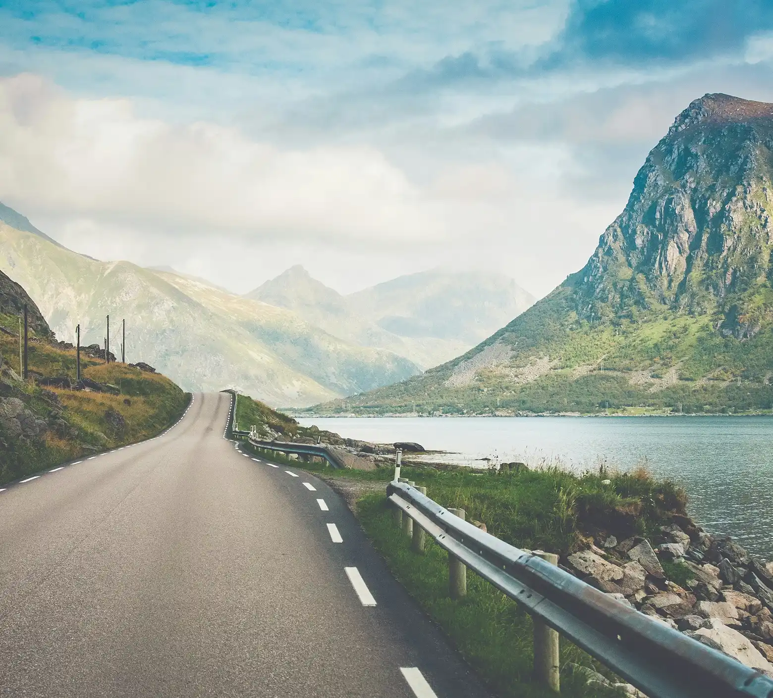 Asphalt road running along a lake with mountains in the background.