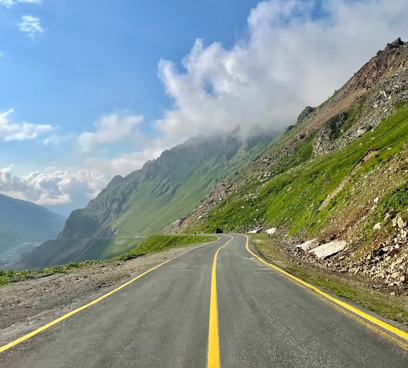 Straight asphalt road crossing the rocky mountain covered by forest.