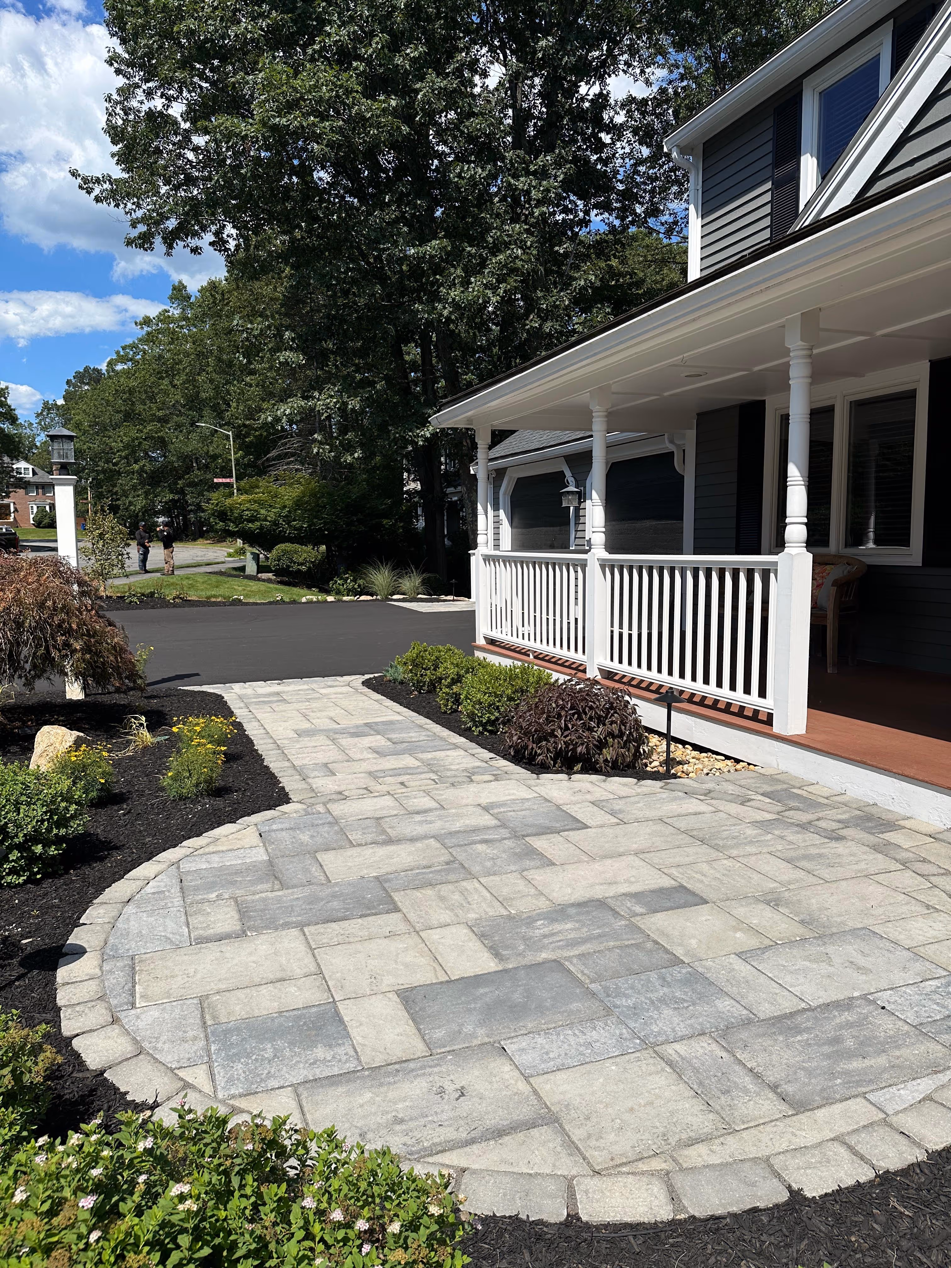 Front porch with white railing and gray paver walkway surrounded by landscaped mulch.