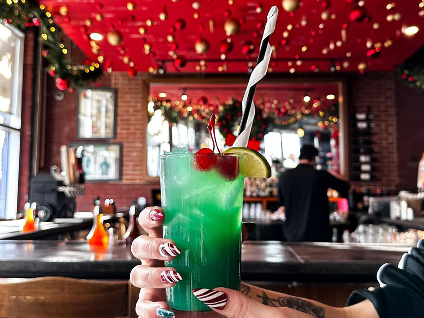a green festive cocktail in front of a bar decorated for Christmas
