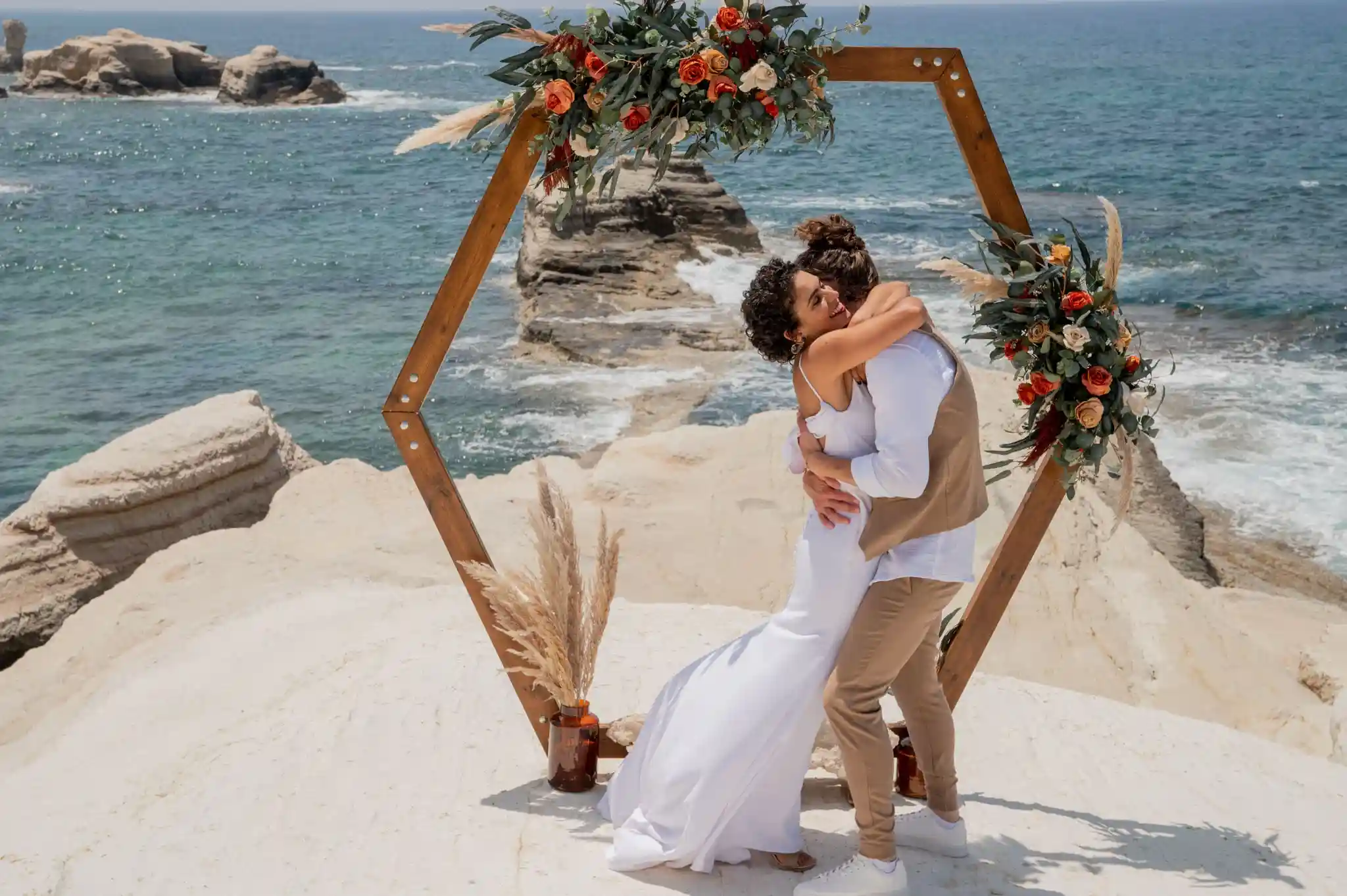 חתן וכלה מתנשקים תחת קשת עץ מול הים במהלך חתונת יעד רומנטית בקפריסין לזוג מישראל