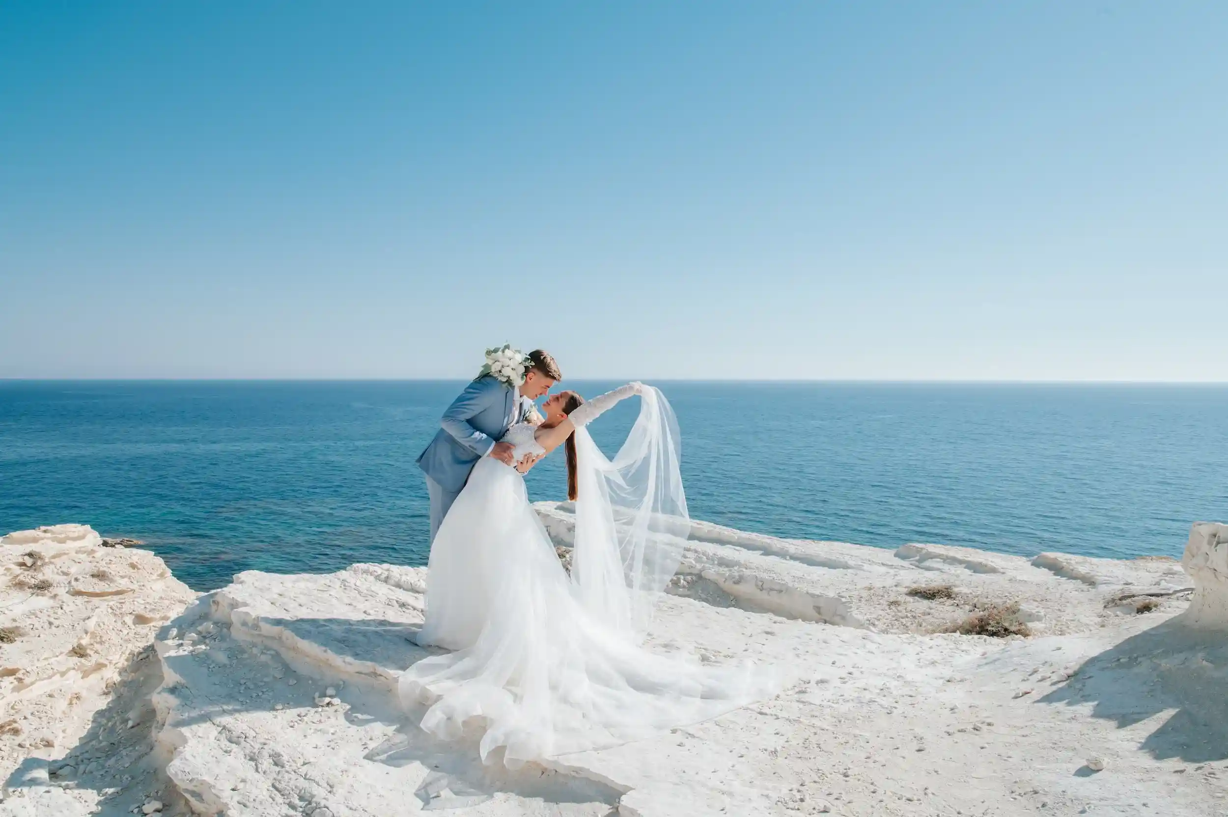 חתן וכלה מתנשקים על צוק מול הים בחתונת יעד רומנטית בקפריסין לזוג מישראל