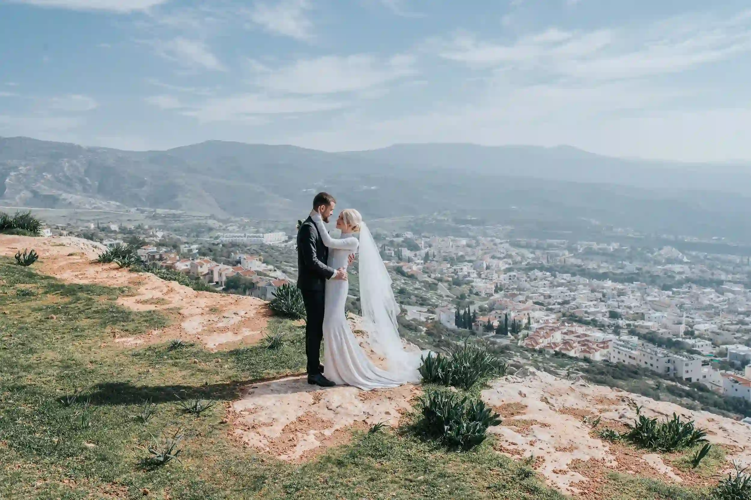 חתן וכלה עומדים על צוק עם נוף לעיר בקפריסין במהלך חתונת יעד רומנטית לזוג מישראל